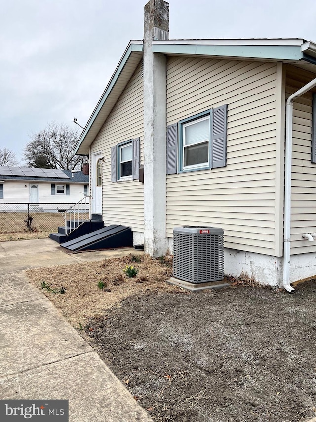 view of side of property featuring central AC unit, a chimney, and fence