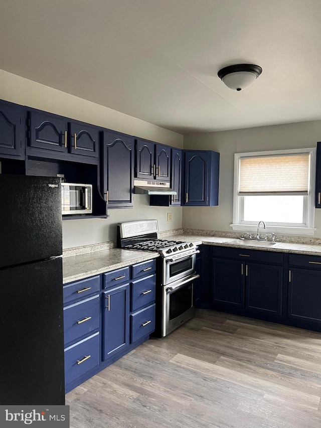 kitchen featuring light wood finished floors, a sink, stainless steel appliances, under cabinet range hood, and blue cabinets