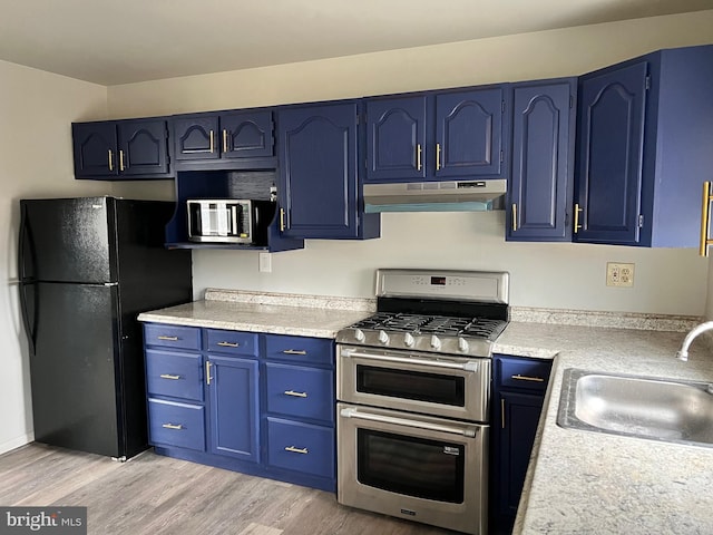 kitchen with blue cabinetry, under cabinet range hood, double oven range, freestanding refrigerator, and a sink