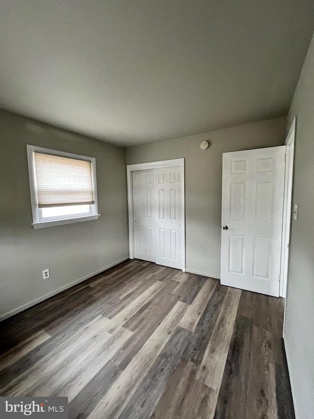 unfurnished bedroom featuring wood finished floors, a closet, and baseboards