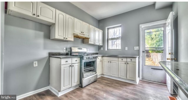 kitchen featuring dark countertops, double oven range, dark wood finished floors, baseboards, and under cabinet range hood