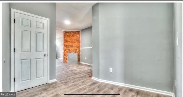 interior space featuring baseboards, a brick fireplace, and light wood-style floors