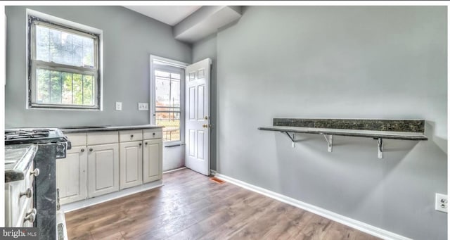 kitchen with dark countertops, wood finished floors, gas range, white cabinets, and baseboards