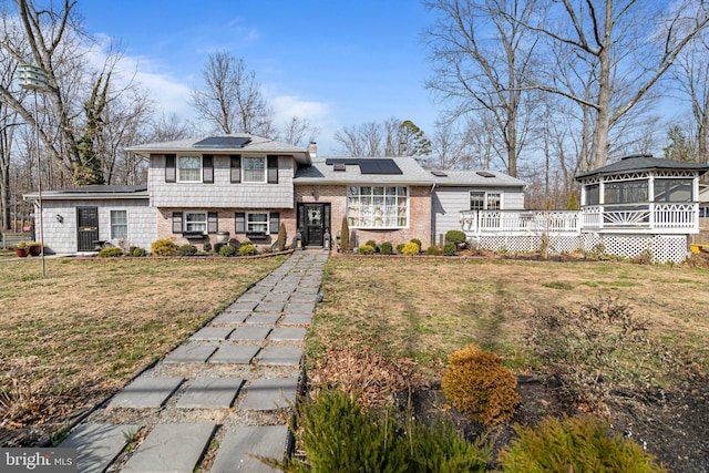 view of front facade featuring a front yard, solar panels, a chimney, a gazebo, and a deck