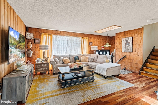 living room with wood walls, a textured ceiling, stairs, and wood finished floors