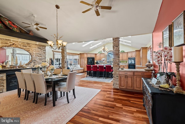 dining space featuring ceiling fan with notable chandelier, light wood-style flooring, decorative columns, and vaulted ceiling