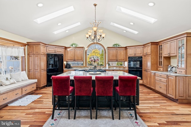 kitchen with a kitchen island, a skylight, light wood-style flooring, black appliances, and a chandelier