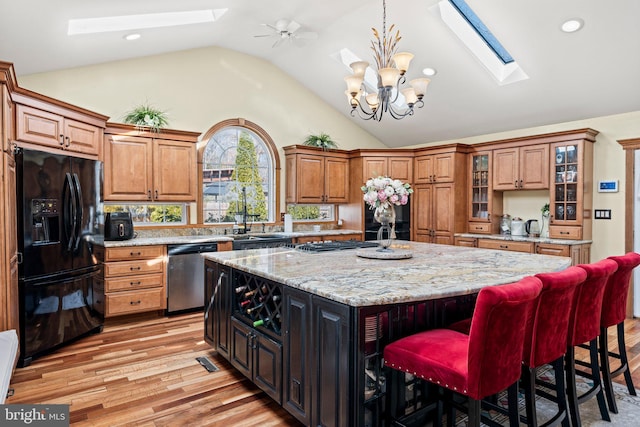 kitchen with brown cabinets, a center island, vaulted ceiling with skylight, appliances with stainless steel finishes, and an inviting chandelier