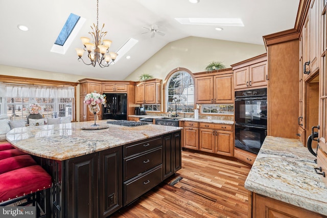 kitchen with a breakfast bar area, light stone counters, vaulted ceiling with skylight, black appliances, and light wood-type flooring