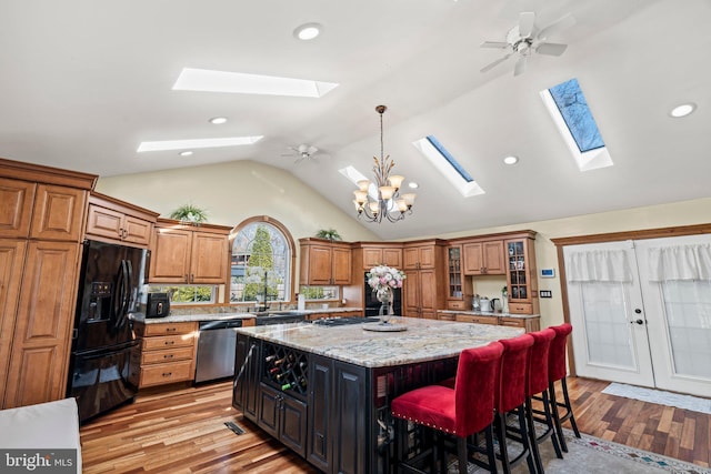 kitchen featuring brown cabinets, black fridge, stainless steel dishwasher, a kitchen island, and a breakfast bar area