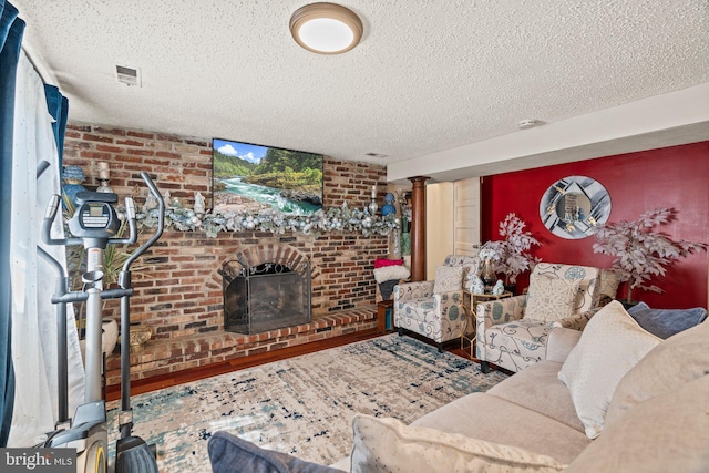 living area featuring a textured ceiling, wood finished floors, brick wall, a brick fireplace, and ornate columns