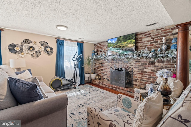 living area featuring a brick fireplace, wood finished floors, visible vents, and a textured ceiling