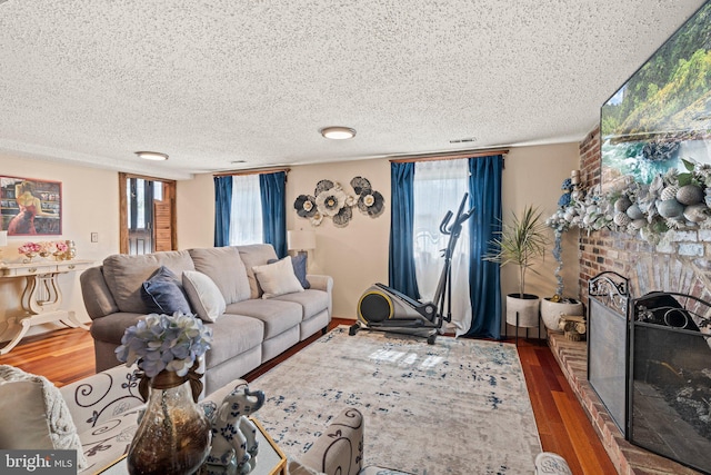 living room featuring visible vents, a fireplace, a textured ceiling, and wood finished floors