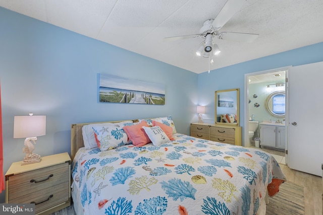 bedroom featuring a sink, a textured ceiling, ensuite bath, wood finished floors, and ceiling fan