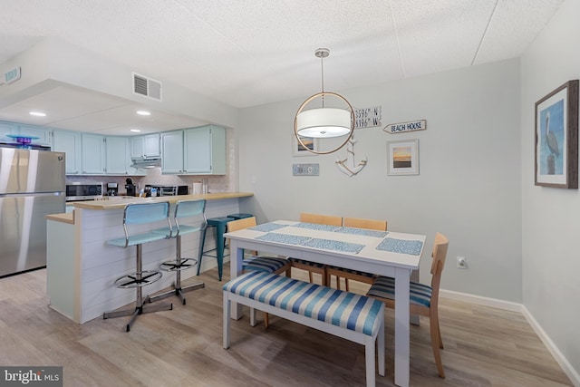 dining room featuring light wood-type flooring, visible vents, baseboards, and a textured ceiling