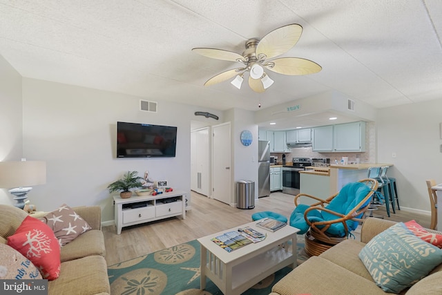 living area featuring light wood-style flooring, a ceiling fan, visible vents, and baseboards