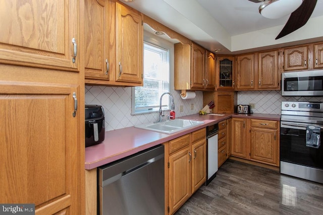 kitchen with brown cabinets, dark wood-type flooring, a sink, tasteful backsplash, and appliances with stainless steel finishes