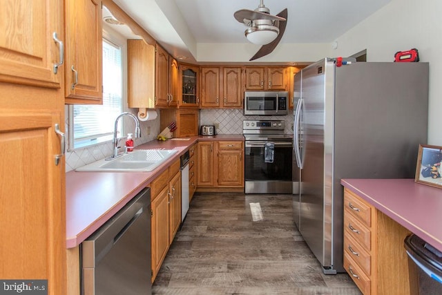 kitchen with a sink, tasteful backsplash, wood finished floors, appliances with stainless steel finishes, and brown cabinetry