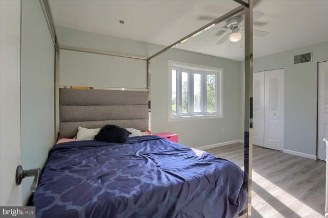 bedroom with a ceiling fan, visible vents, wood finished floors, baseboards, and multiple closets