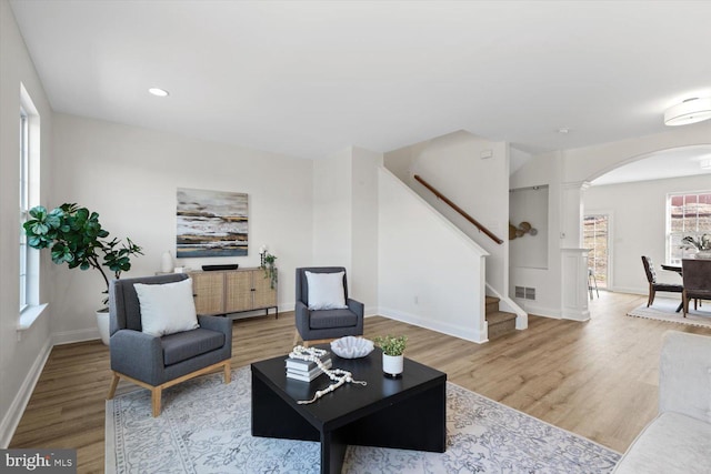 living area featuring arched walkways, visible vents, stairs, and wood finished floors