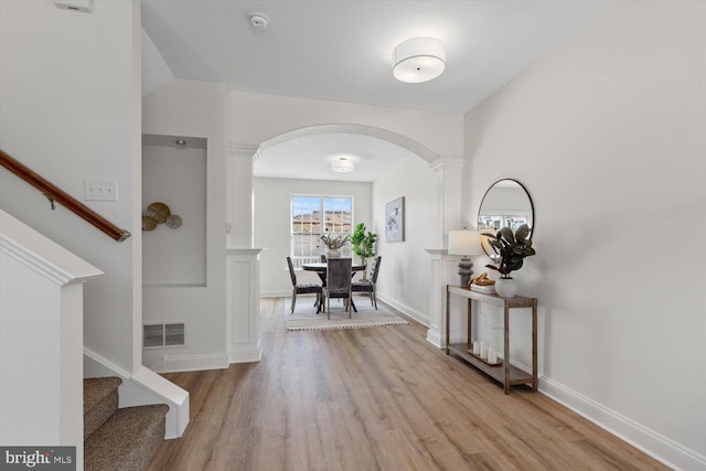 entryway with arched walkways, stairway, baseboards, and wood finished floors