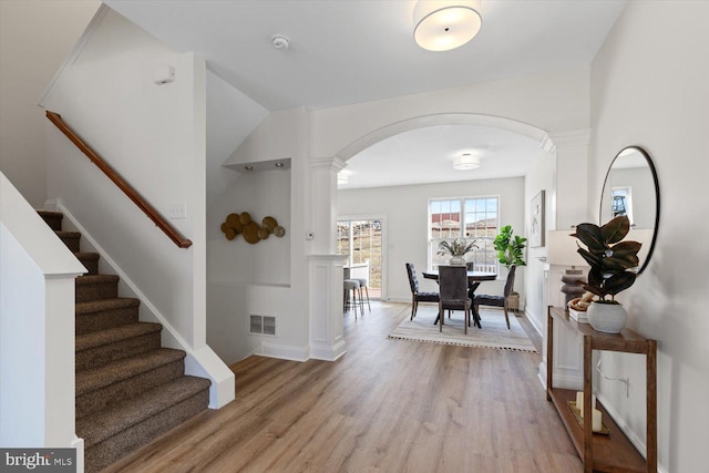 entrance foyer featuring light wood-type flooring, visible vents, stairway, arched walkways, and decorative columns