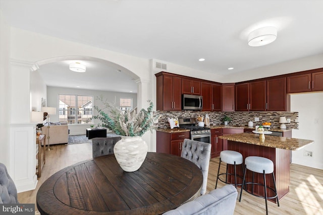 kitchen featuring visible vents, dark brown cabinets, open floor plan, arched walkways, and stainless steel appliances