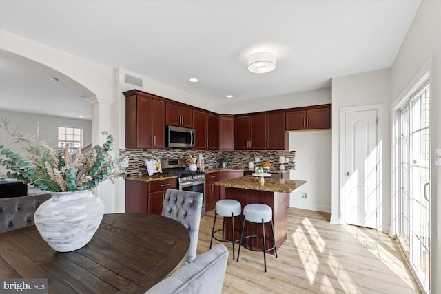 kitchen featuring visible vents, arched walkways, stainless steel appliances, open floor plan, and reddish brown cabinets