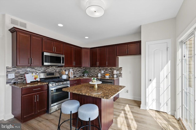 kitchen with light wood finished floors, visible vents, stainless steel appliances, and reddish brown cabinets