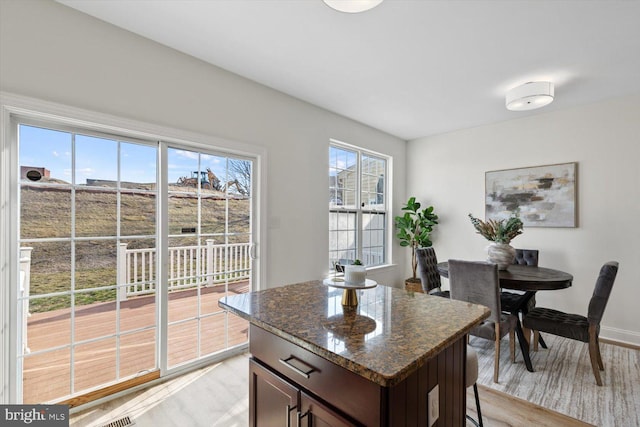 kitchen with dark stone countertops, dark brown cabinets, baseboards, and light wood finished floors