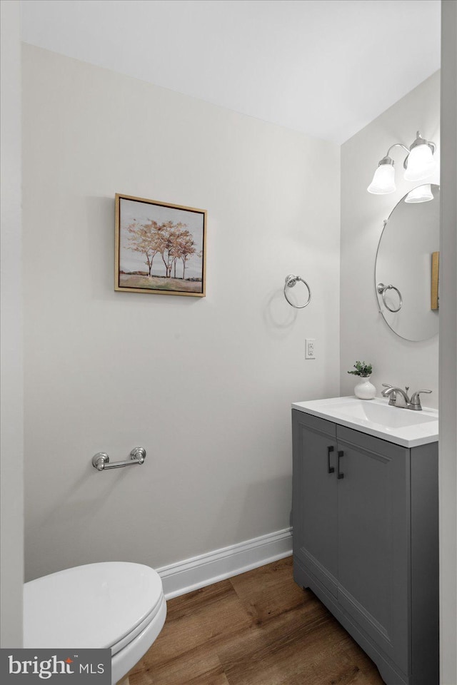 half bathroom with baseboards, toilet, wood finished floors, and vanity