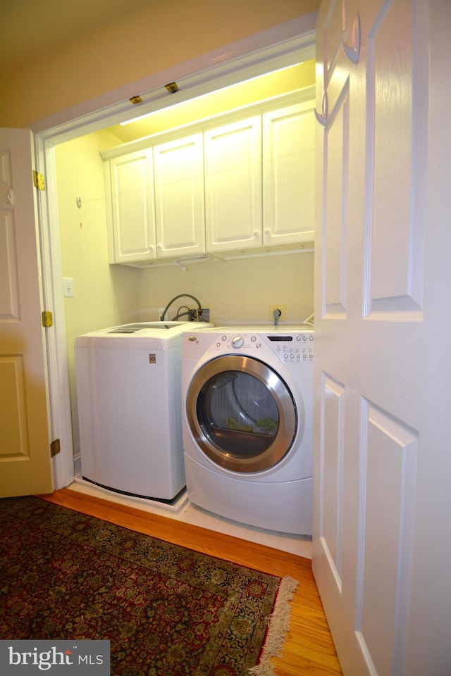 washroom with cabinet space, light wood-type flooring, and washing machine and clothes dryer