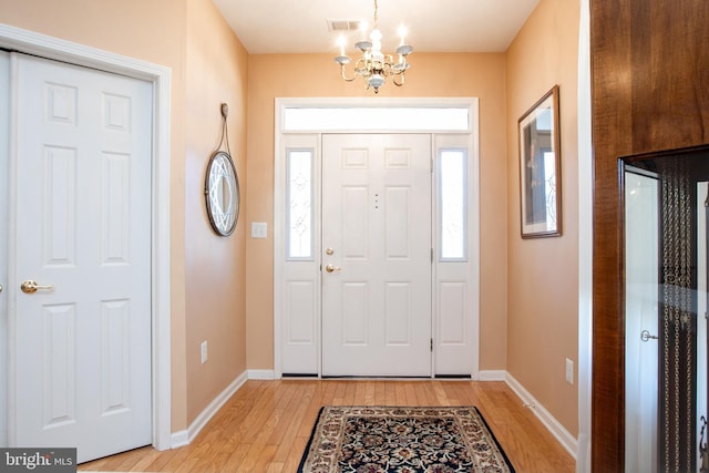 entryway with an inviting chandelier, light wood-style flooring, visible vents, and baseboards