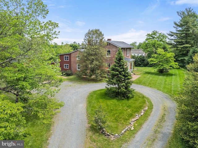view of front facade featuring curved driveway, a chimney, and brick siding