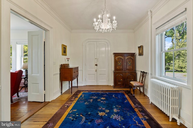 foyer entrance featuring radiator heating unit, hardwood / wood-style floors, a chandelier, and ornamental molding