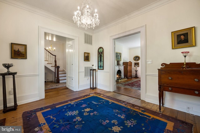 entrance foyer featuring a chandelier, wood-type flooring, stairway, crown molding, and a lit fireplace