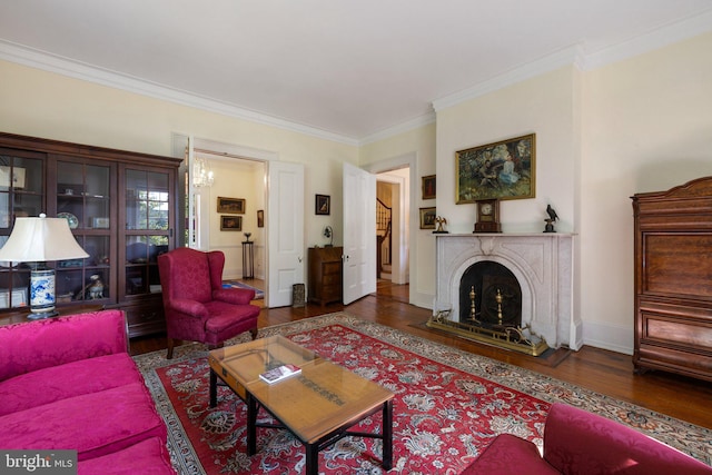 living area featuring wood finished floors, crown molding, a fireplace with raised hearth, baseboards, and a chandelier