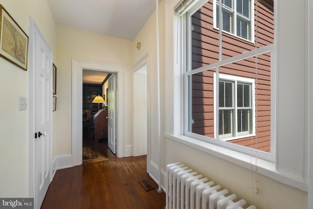 corridor with dark wood-style floors, radiator heating unit, and baseboards