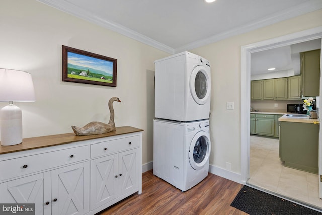 laundry room featuring stacked washing machine and dryer, crown molding, baseboards, light wood finished floors, and recessed lighting