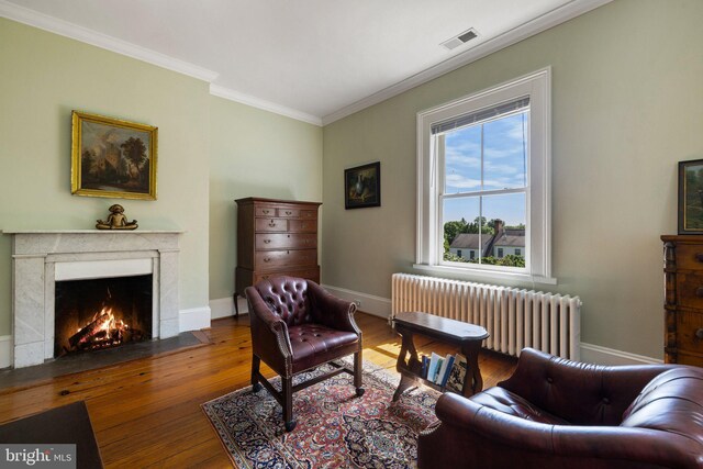 living area featuring radiator heating unit, crown molding, wood-type flooring, a premium fireplace, and baseboards