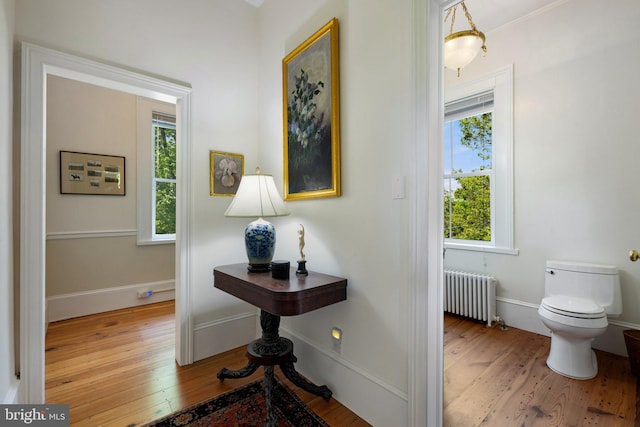 hallway with radiator heating unit, wood finished floors, and baseboards