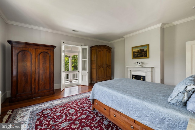 bedroom with wood finished floors, crown molding, a fireplace, and baseboards