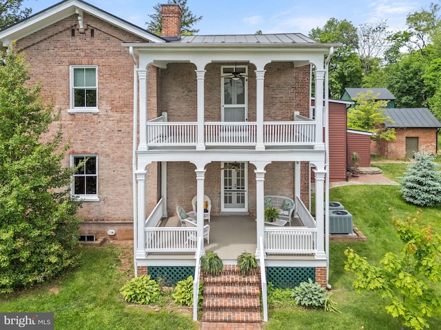 view of front of home with a balcony, a chimney, brick siding, cooling unit, and a front yard