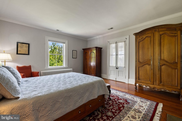 bedroom with radiator heating unit, wood finished floors, crown molding, and baseboards