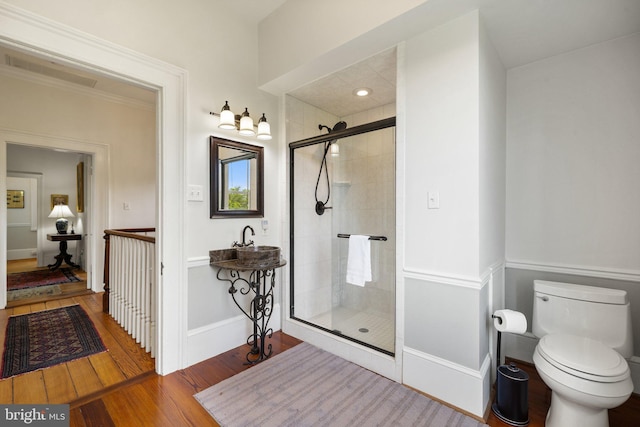bathroom with wood finished floors, a shower stall, toilet, and baseboards