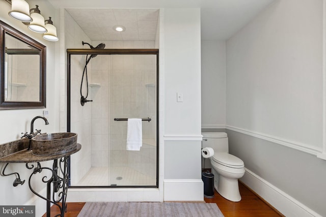 bathroom featuring a stall shower, toilet, wood finished floors, a sink, and baseboards