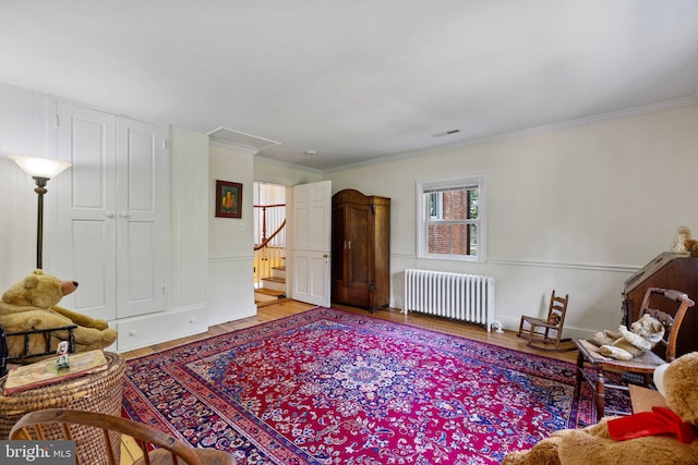 living area with radiator heating unit, wood finished floors, crown molding, attic access, and stairs