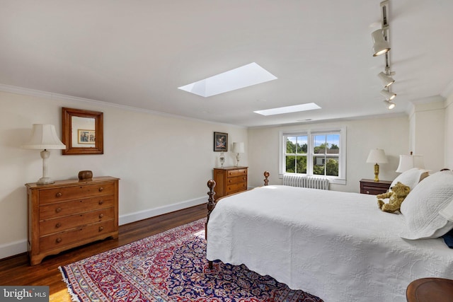 bedroom featuring a skylight, crown molding, wood finished floors, track lighting, and baseboards