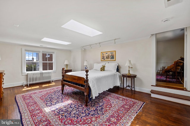 bedroom featuring radiator, a skylight, hardwood / wood-style floors, rail lighting, and baseboards