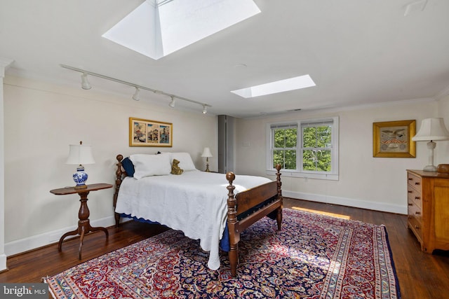 bedroom featuring a skylight, rail lighting, dark wood finished floors, crown molding, and baseboards